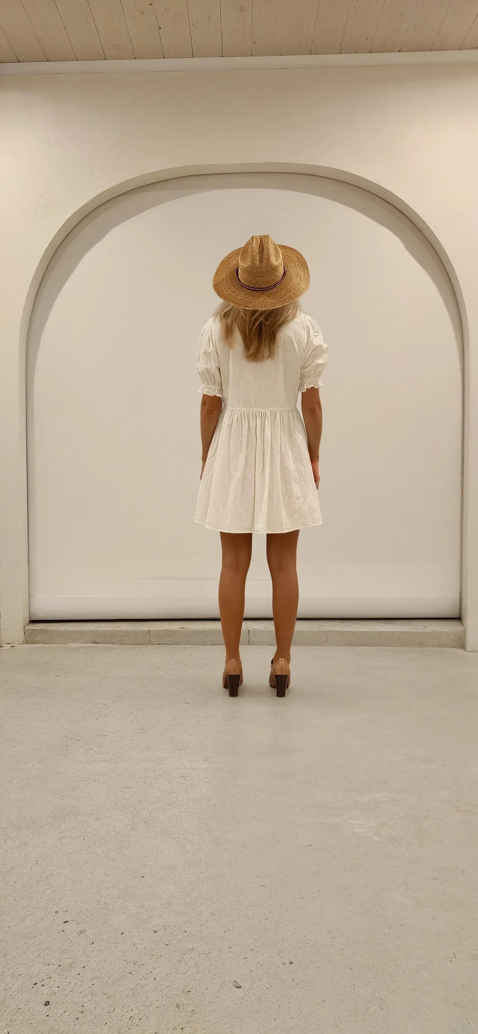 Full rear view of the Mara Mini dress worn with a straw hat and tan heels, styled in a relaxed neutral space.