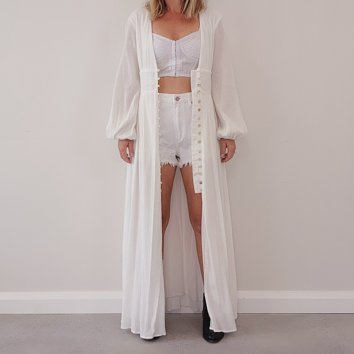 White button-down maxi dress worn open as a duster, styled over a white crop top and white cut off shorts.