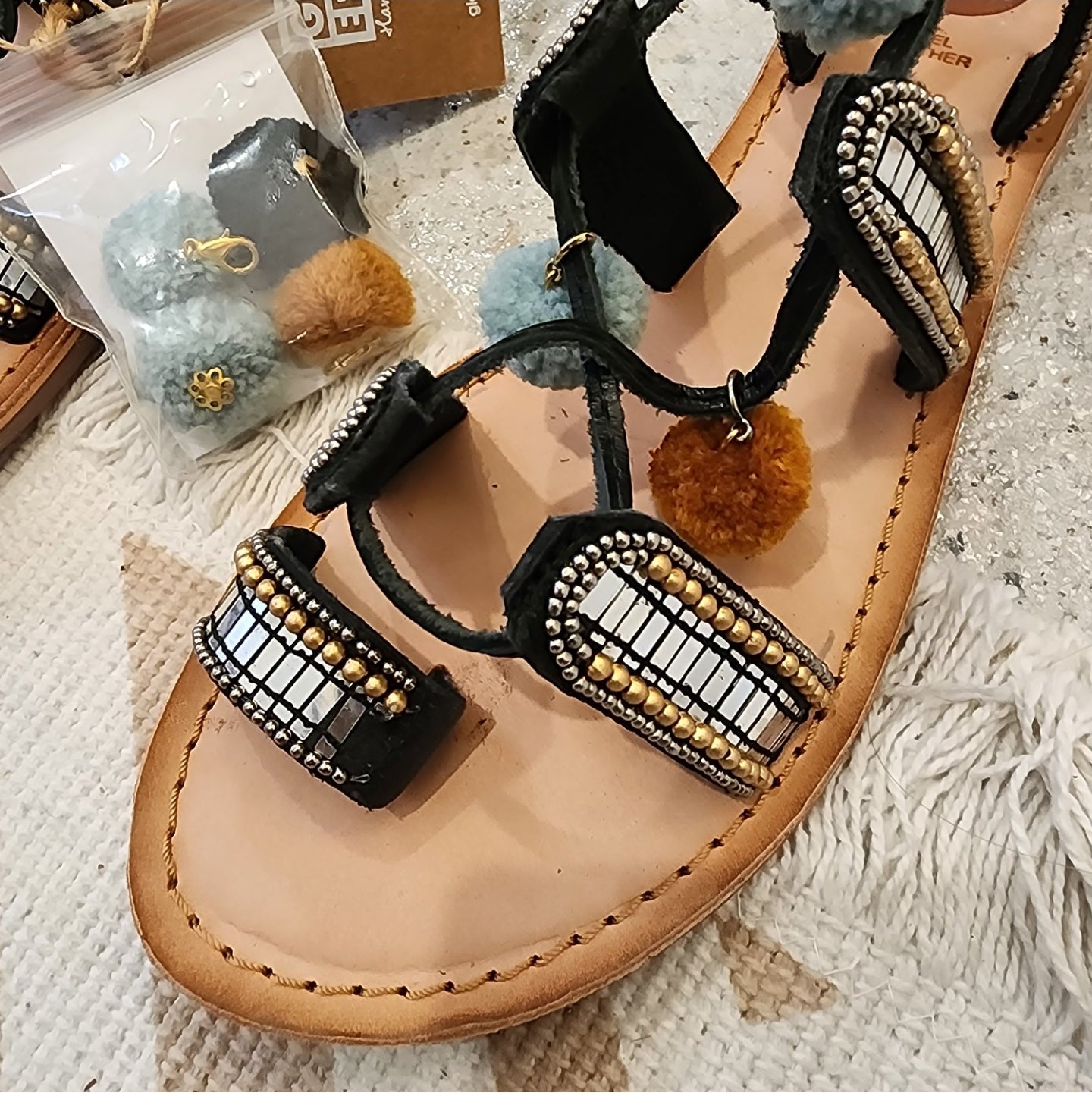 Gioseppo Nayeli sandal with mirror and pom pom details and tan leather wrap-around straps, close up viewing shoing missing mirror.