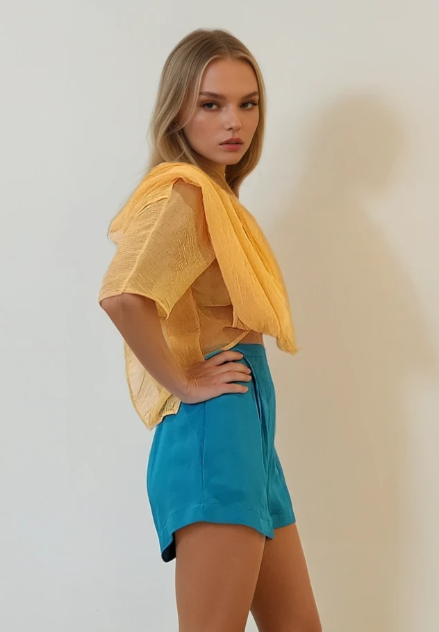 Side profile of the Johansen top styled with blue shorts, showcasing the draped front-tie silhouette.