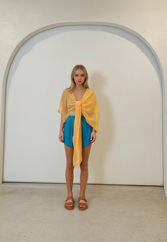 Model wears a mango-orange Johansen Haze top threaded through the front, styled with vibrant blue Zimmermann shorts. Full-length front view.