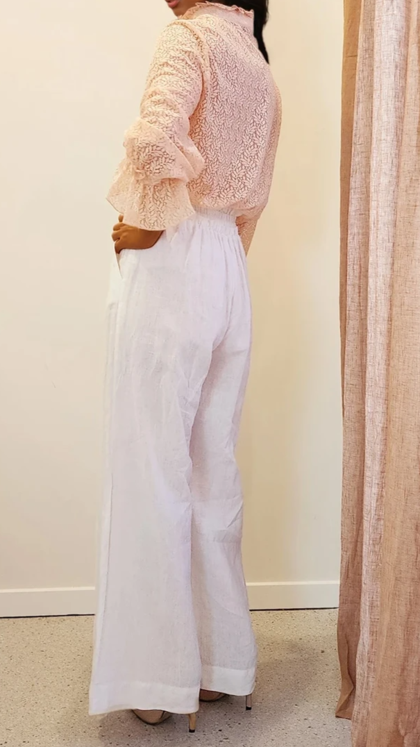 Side view of the model glancing over her shoulder, showing the soft texture and sleeve detail of the Oskar lace top in muted peach.