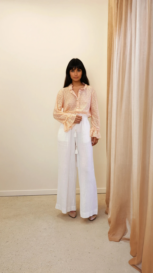 Model wearing the Oskar peach lace top facing front, tucked into high-waisted white pants with flared sleeves on display.