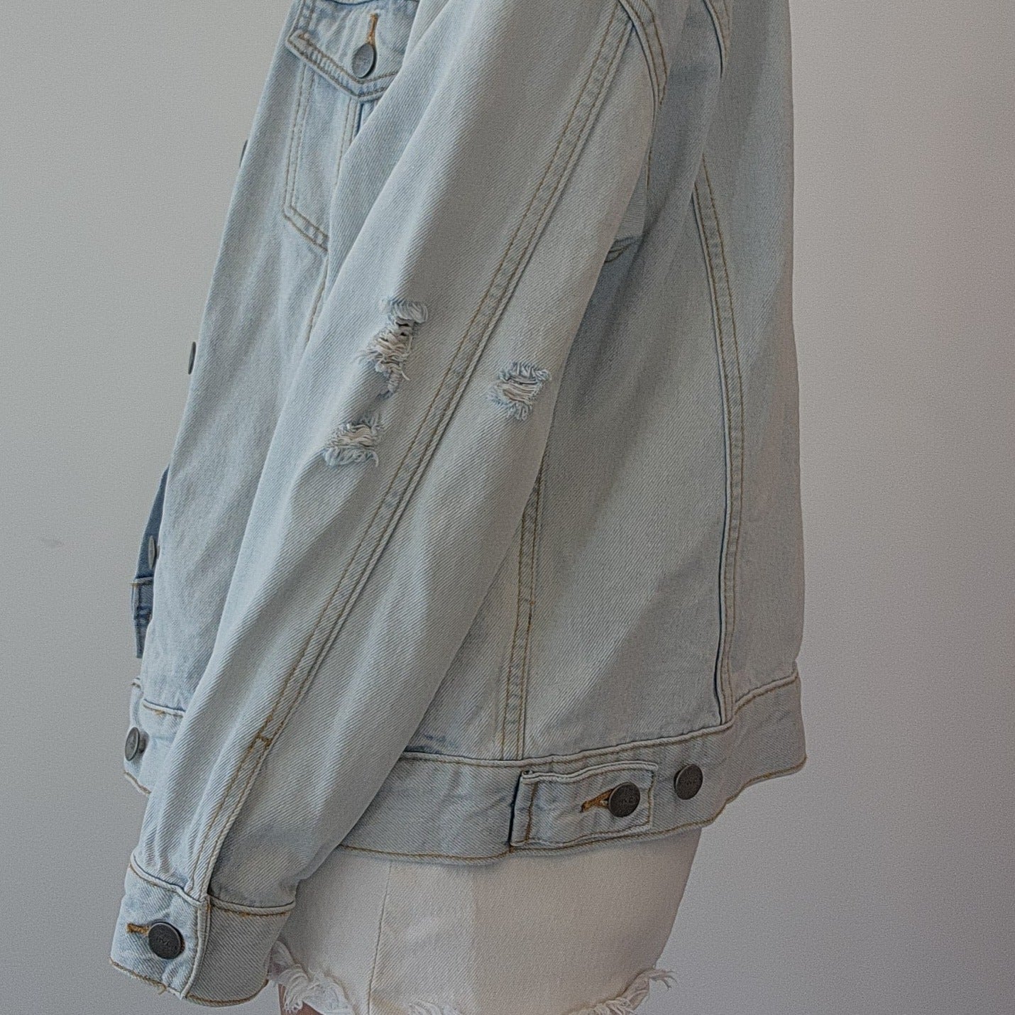 Side view of a model showing the factory distress on a light wash denim button up jacket by clothing designer RVCA
