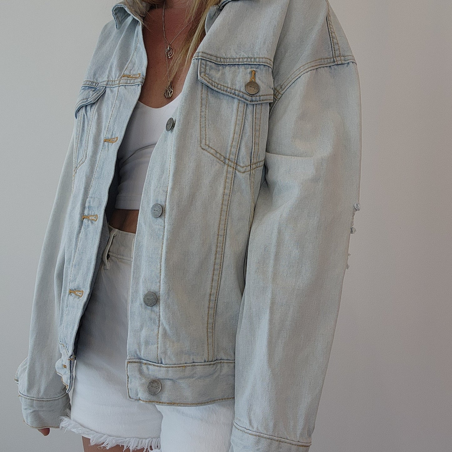 Side profile of model wearing RVCA denim jacket, paired with denim shorts and a crop top. size S