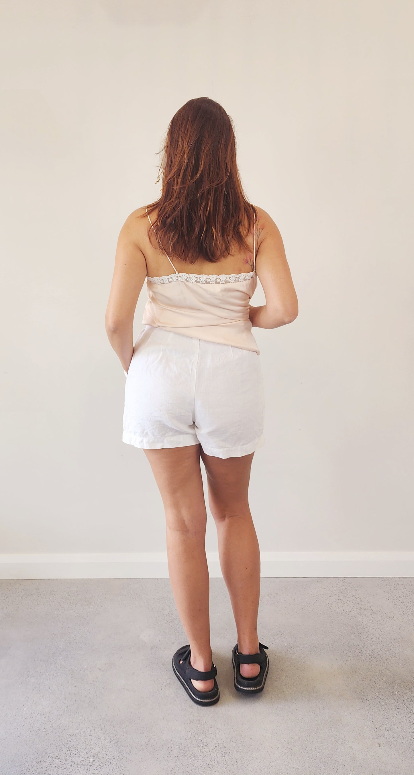 Model wearing the St Agni white linen shorts, showing the back view.