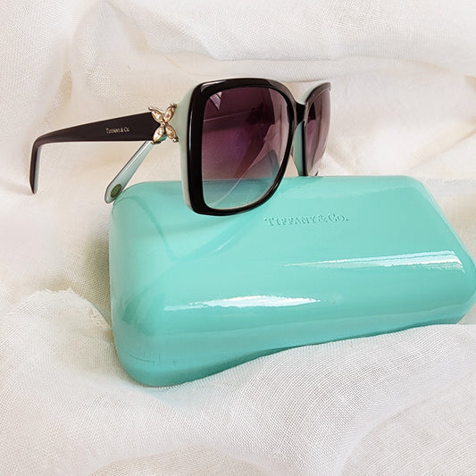 Close up of side of Tiffany and Co. sunglasses showing crystal side detail and sunglasses case in aqua.