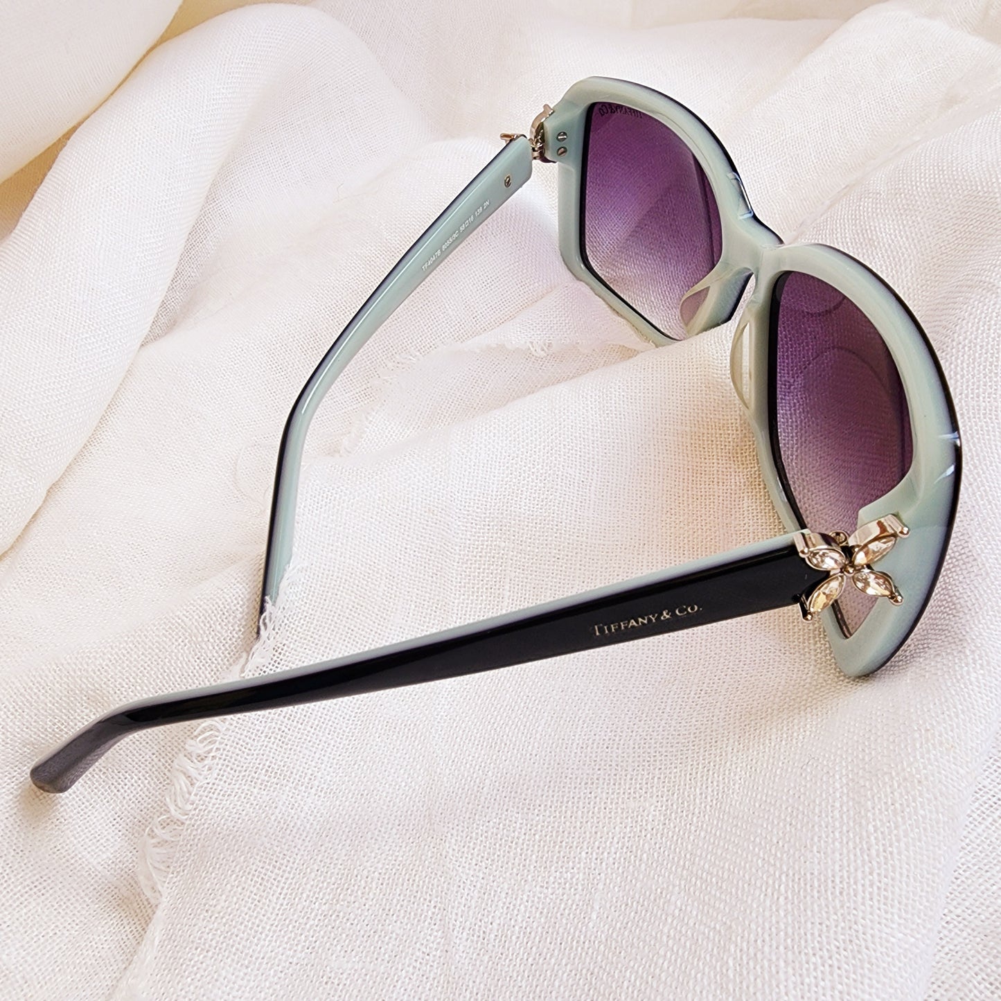Close up of the right side of the authentic Tiffany & Co sunglasses showing the black and aqua frame and Swarovski crystal side detail.
