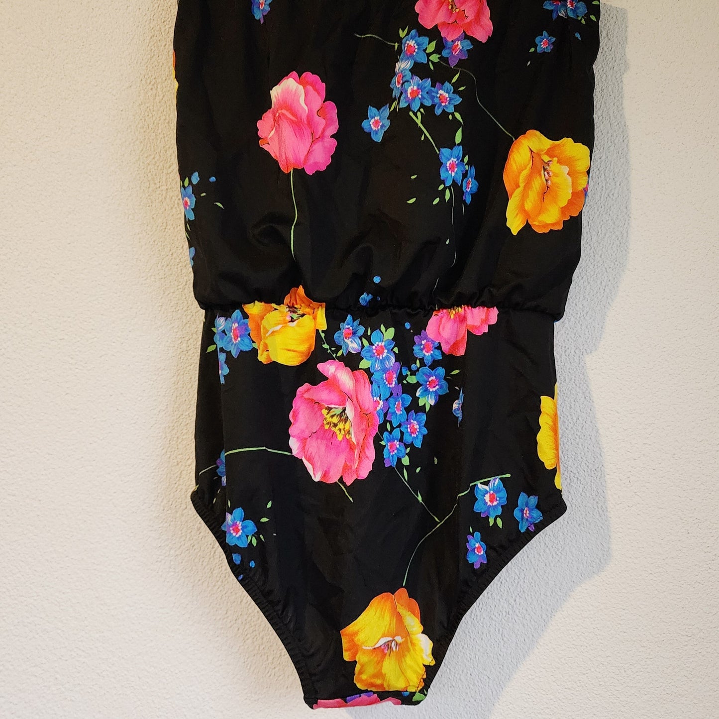 Back view of vintage black swimsuit with a colourful floral design on a white surface