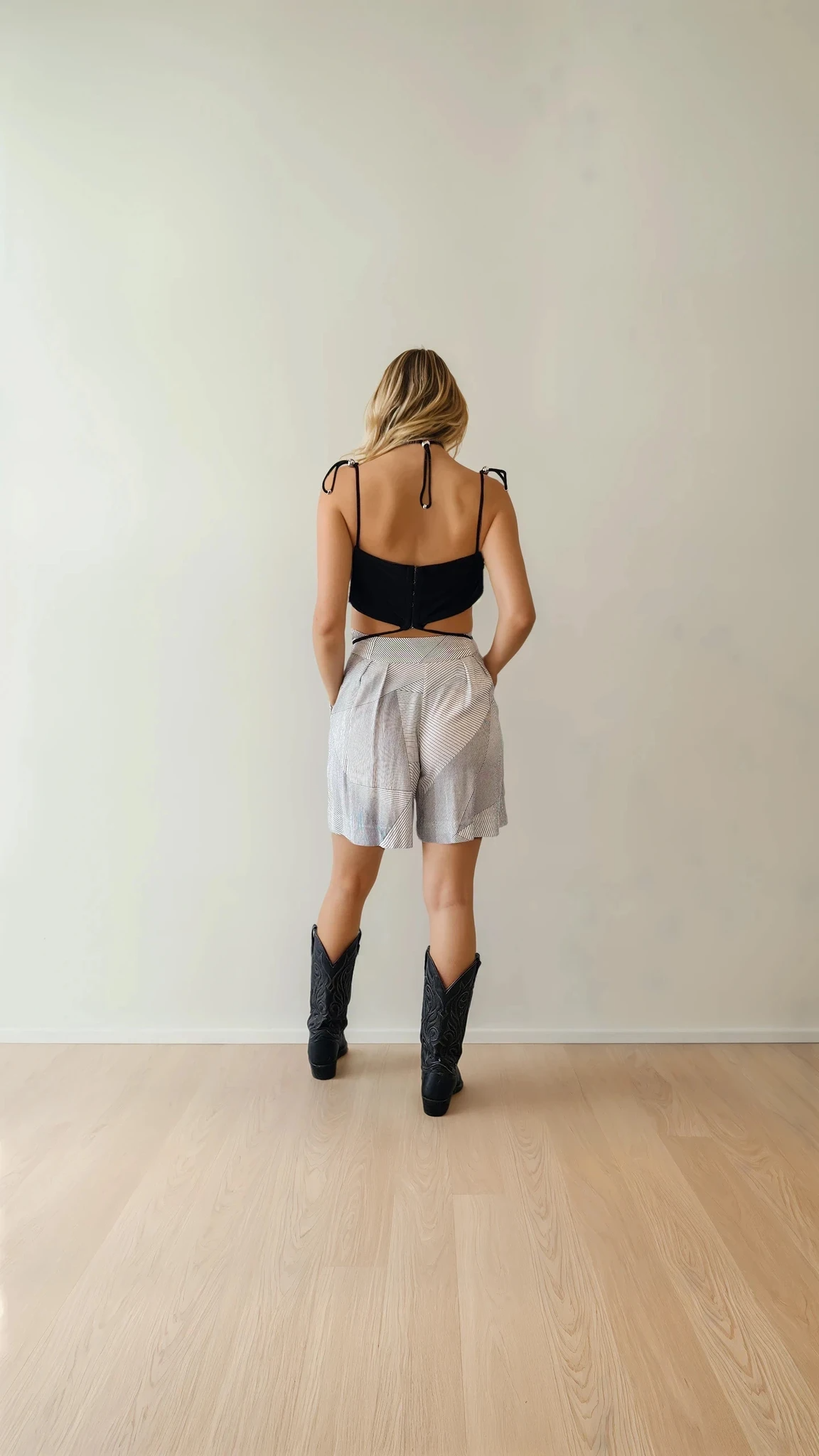 Model facing away from the camera wearing high-waisted Zimmermann shorts with subtle panel detailing, paired with a black Dion Lee crop top and western boots.