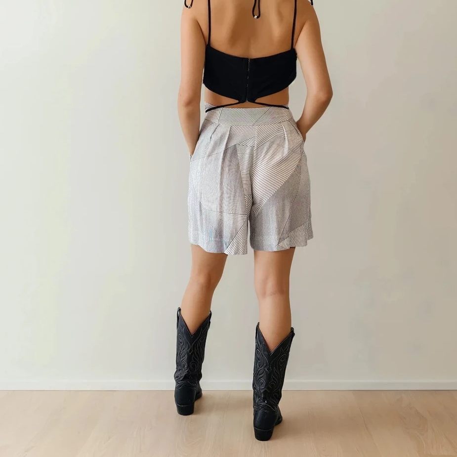 Model facing away from the camera wearing high-waisted Zimmermann shorts with subtle panel detailing, paired with a black Dion Lee crop top and western boots.
