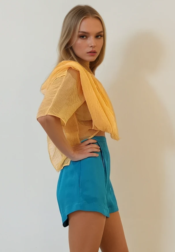 Side angle of Zimmermann blue silk shorts highlighting the pleated detail and length on model.