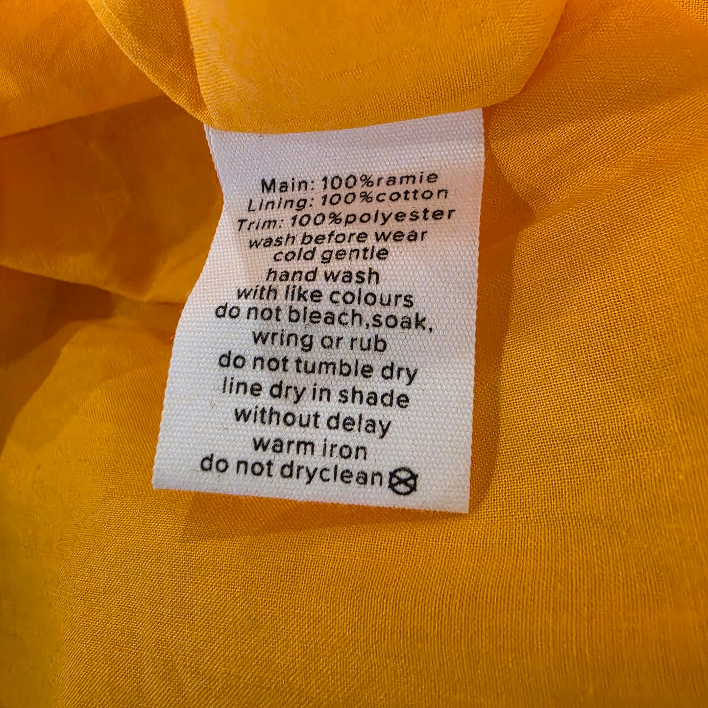 A close-up of a white fabric care label sewn onto the Aere cut out dress, showing care instructions.