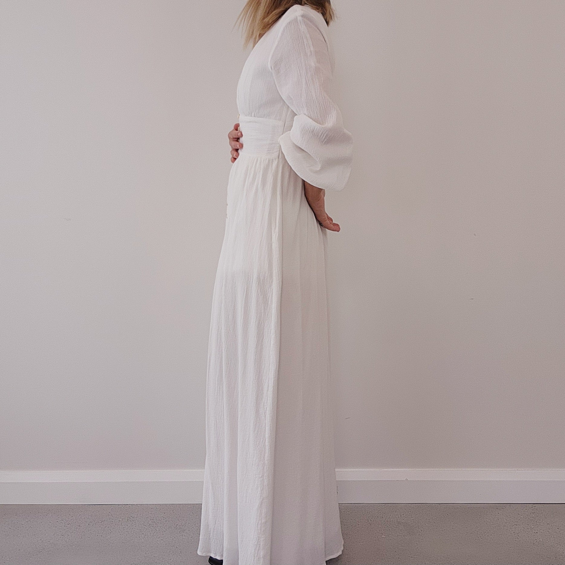 Side profile of white flowy maxi dress with flattering waist and long sleeves
