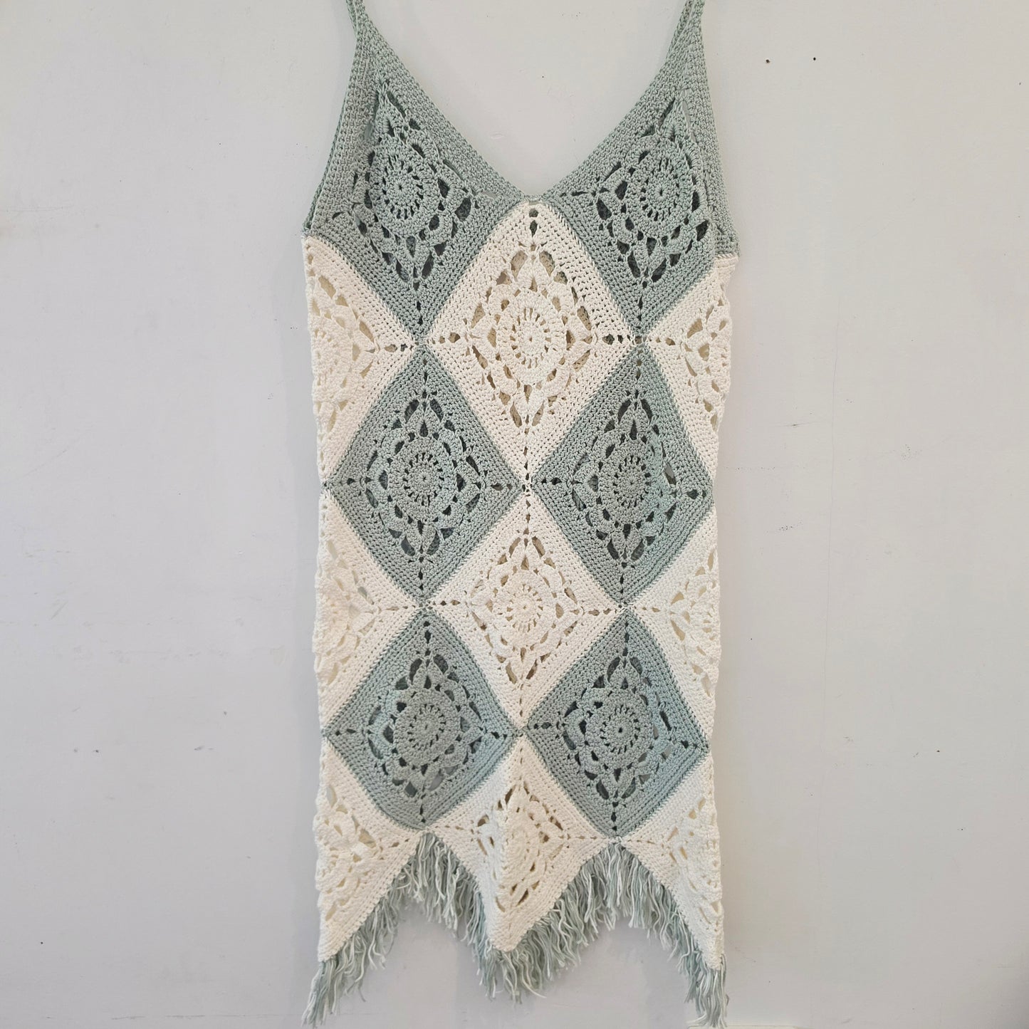 Flat lay of the crochet fringe dress in green & white with a fringe hemline.