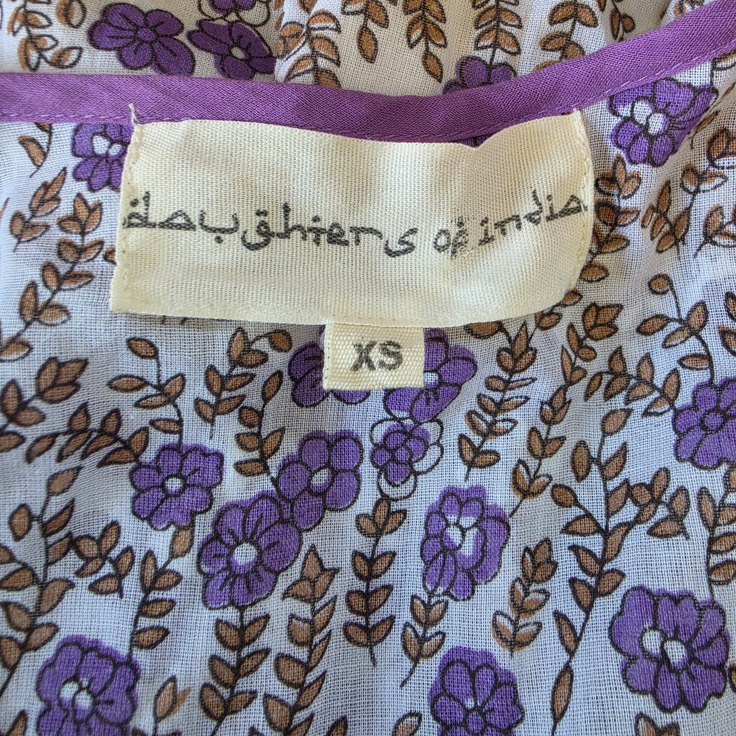 Close-up of a fabric garment showing the size label that reads 'daughters of india' and 'XS
