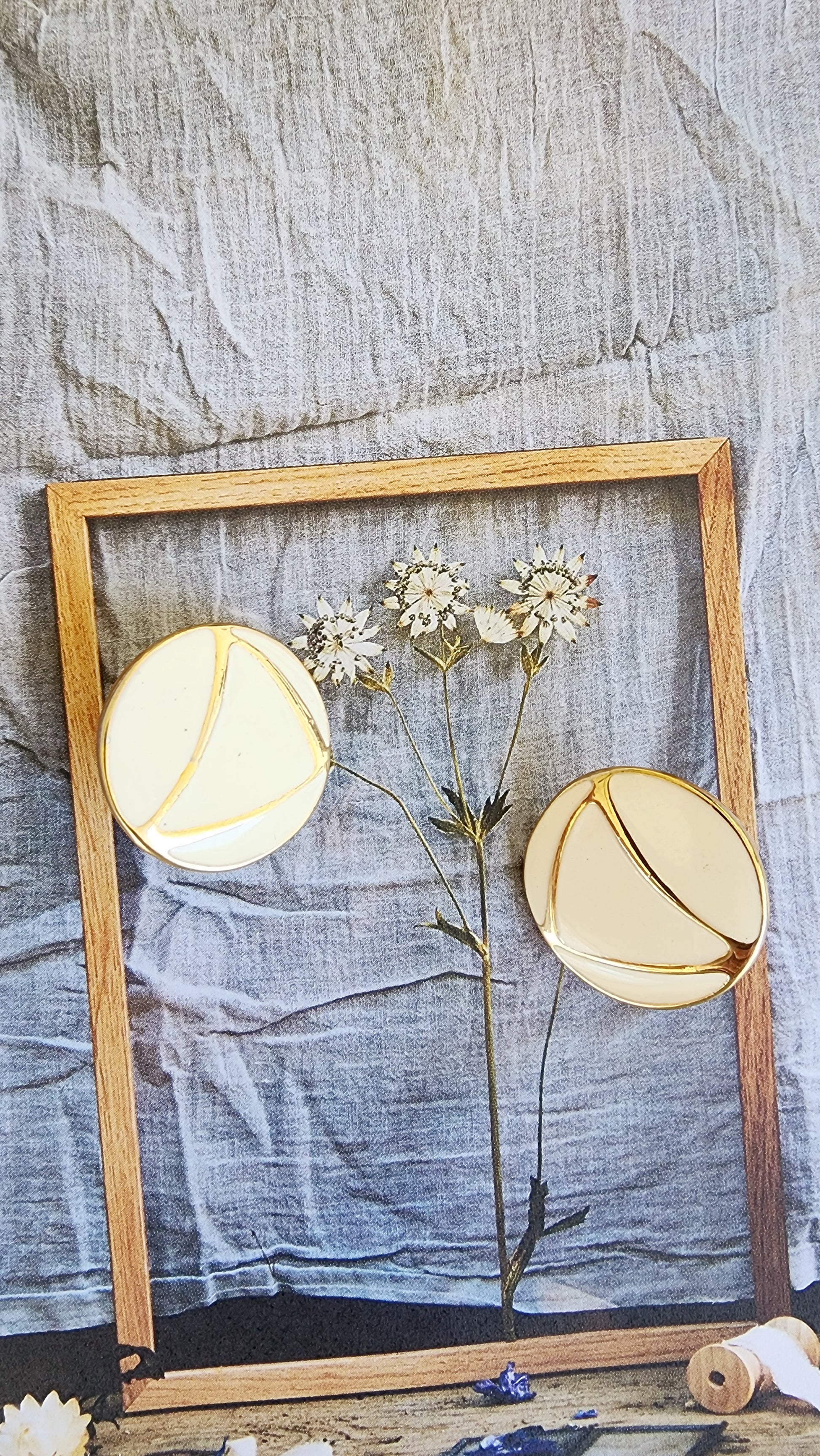 Styled image of round enamel earrings on pressed botanical print with linen backdrop