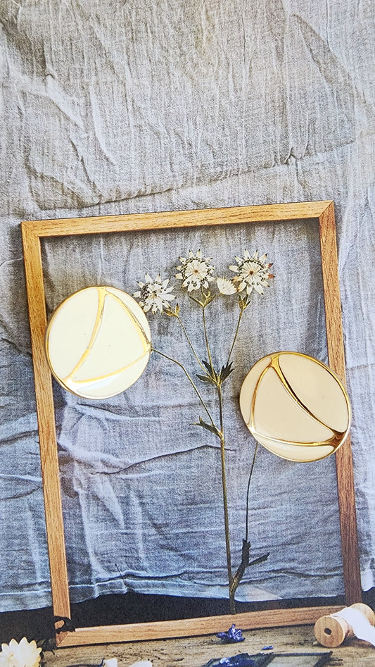 Styled image of round enamel earrings on pressed botanical print with linen backdrop