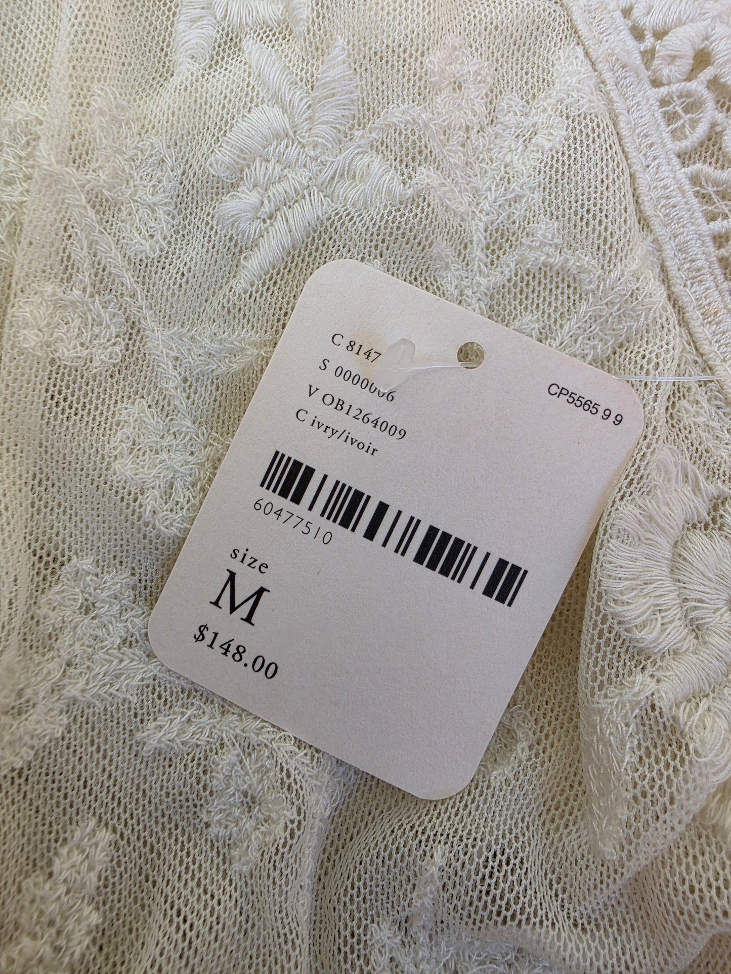 A close-up of white lace dress with a product tag attached, size M, and price $148.00.