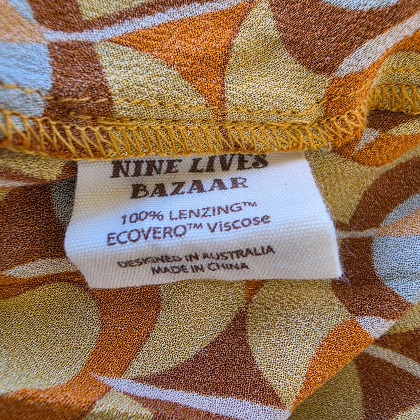 Close-up of the Quincy Dress with a sewn-in label reading 'NINE LIVES BAZAAR' and '100% LENZING ECOVERO Viscose'. The fabric has an abstract geometric pattern.