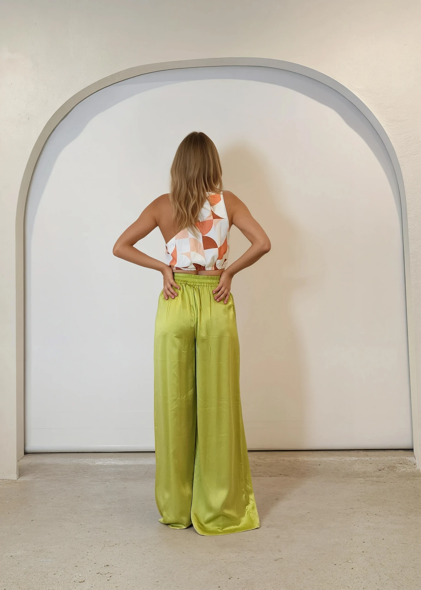 Back view of model wearing lime green Palm Swimwear Happy Pants with a printed asymmetric crop top.