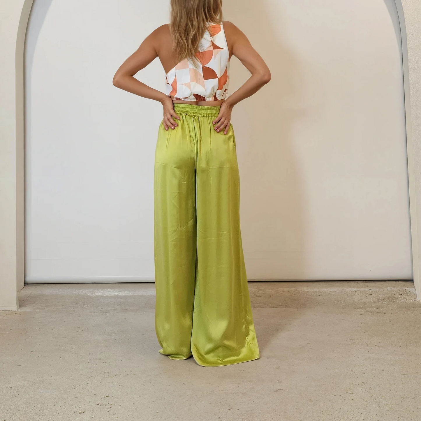 Back view of model wearing lime green Palm Swimwear Happy Pants with a printed asymmetric crop top.
