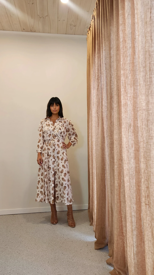 Model facing forward wearing R.M. Williams silk ruffle dress in cream with tan floral print, puffed sleeves and tiered skirt.