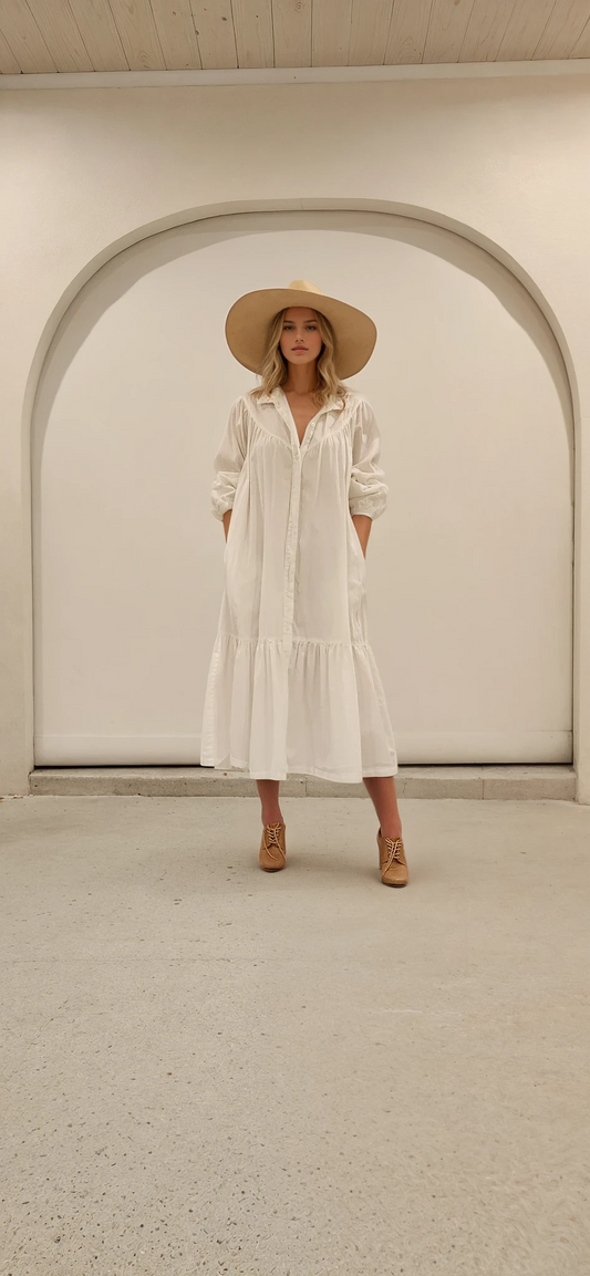 Model wearing long sleeve white cotton maxi dress with button front, standing in arched doorway