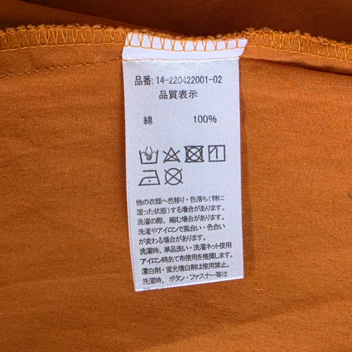 A close-up of a garment care label with Japanese text and washing symbols, sewn onto the rust ruffle blouse.