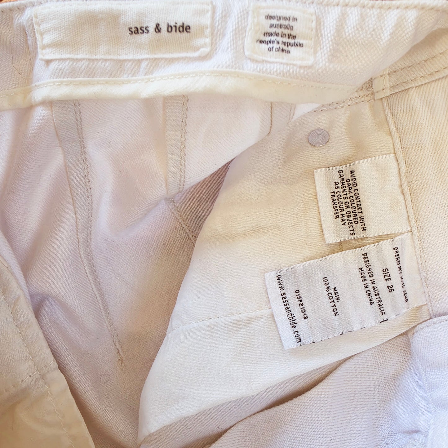 Close-up of the interior waistband and tags of off-white denim jeans, showing the 'sass & bide' brand label and care instructions.