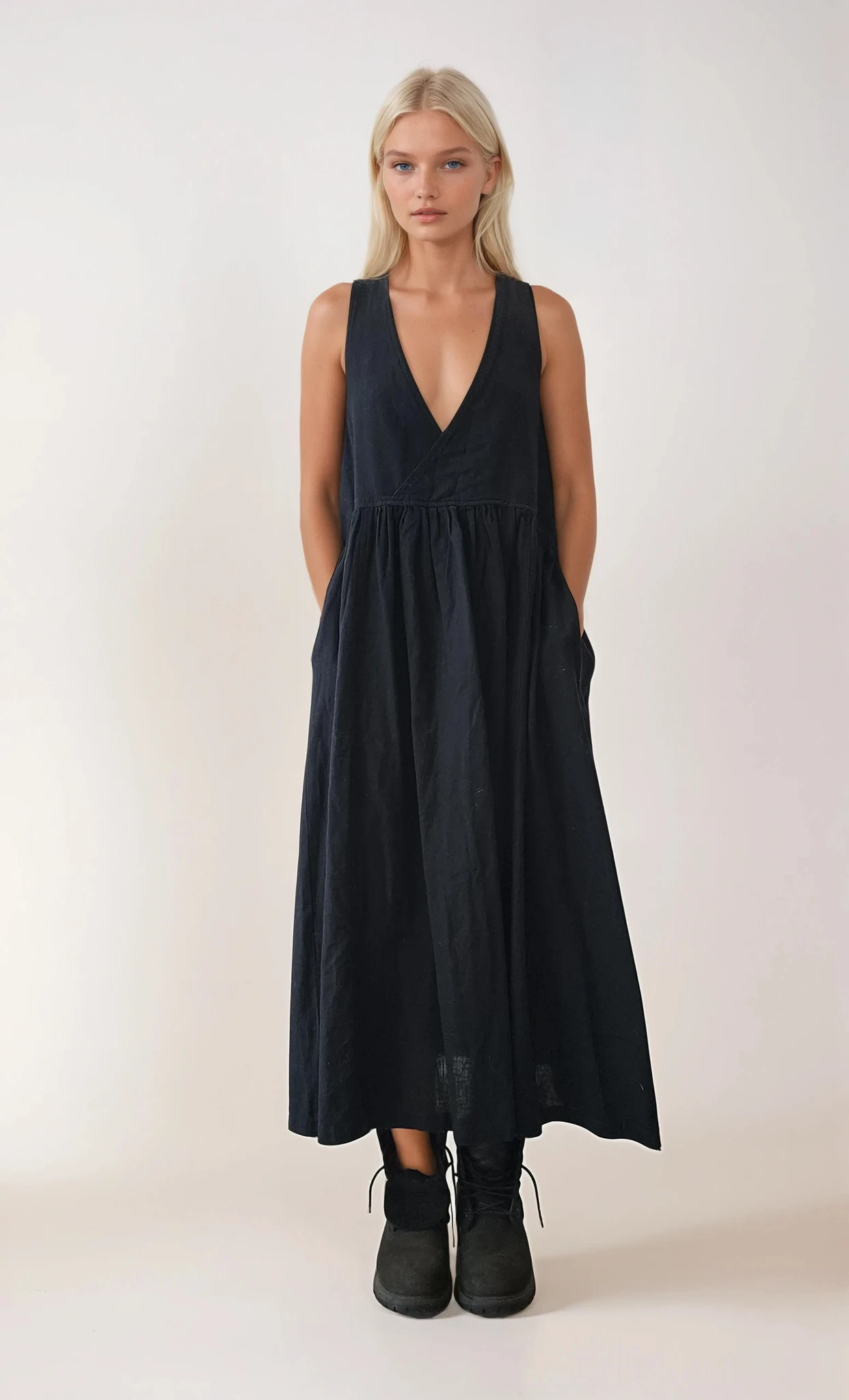 Black sleeveless pinafore midi dress with deep V neckline and gathered waist, worn front-facing.