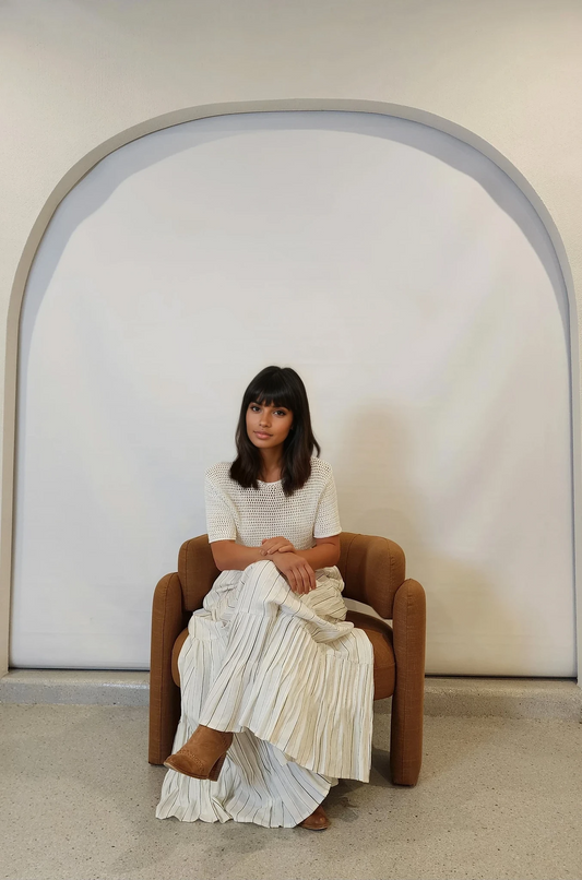 Model seated with legs crossed, wearing the linen skirt styled with tan boots and white crochet top.