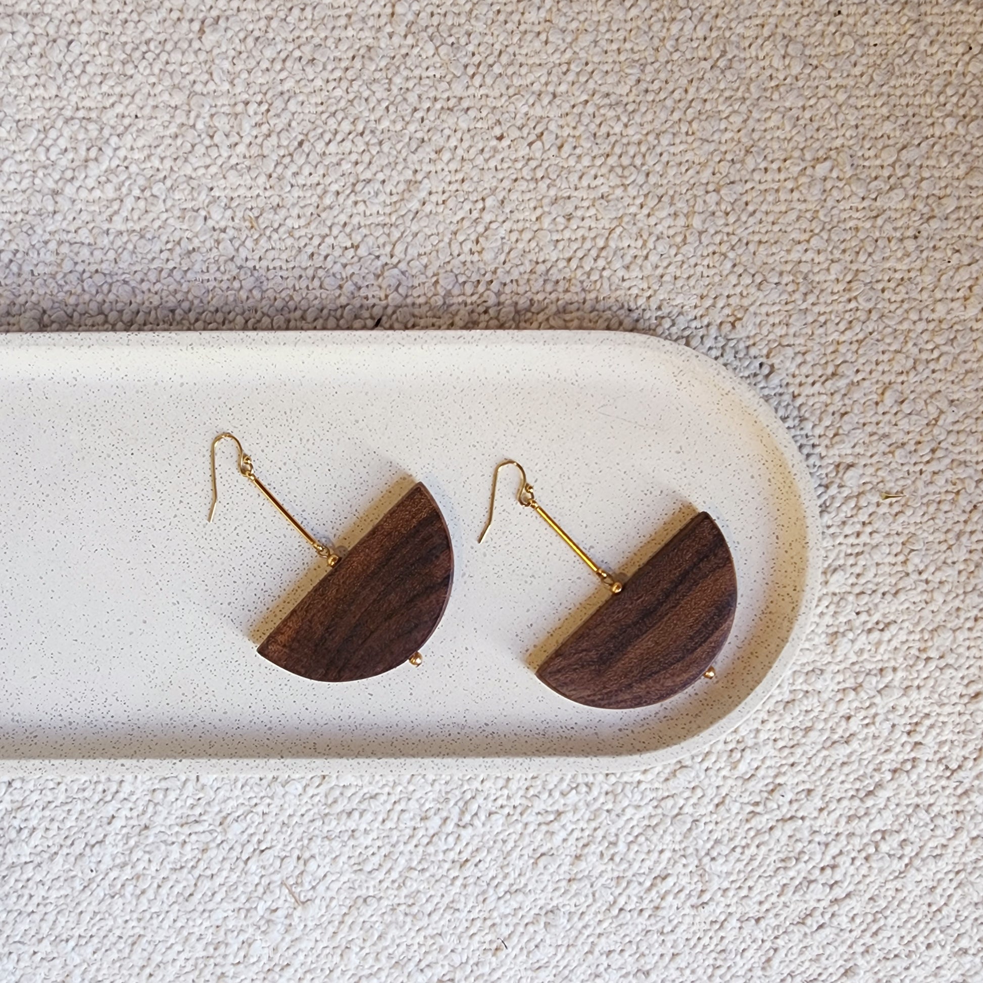 A close up view of the wooden, handmade Cassie earrings, showing the half moon shape with gold plated hardware.