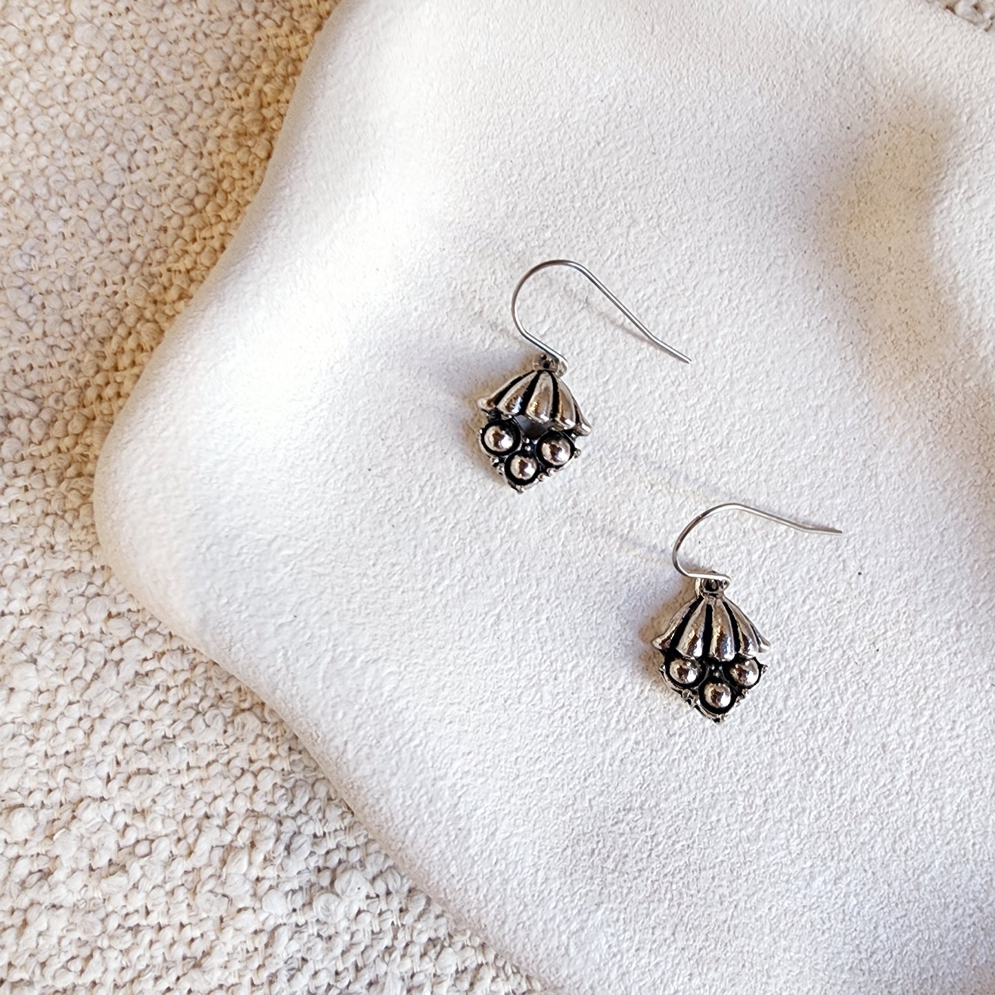 Martinia earrings with silver drop charm and stainless steel hook on white textured surface