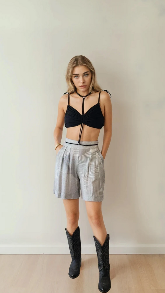 Front-facing view of model in monochrome Zimmermann shorts with tailored pleats and angled pockets, styled with a black Dion Lee crop top and cowboy boots.