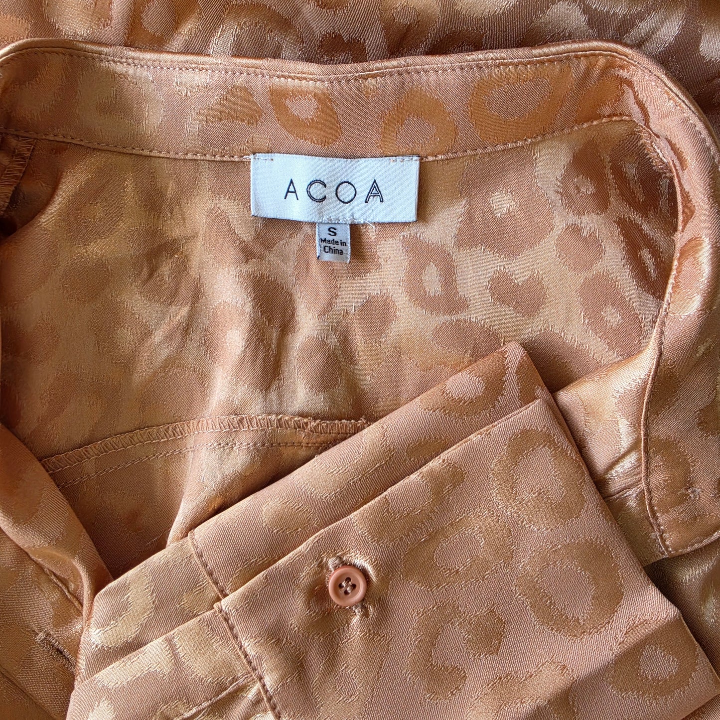 Close-up view of the brand label and shiny animal print pattern on the ACOA retro button up shirt.