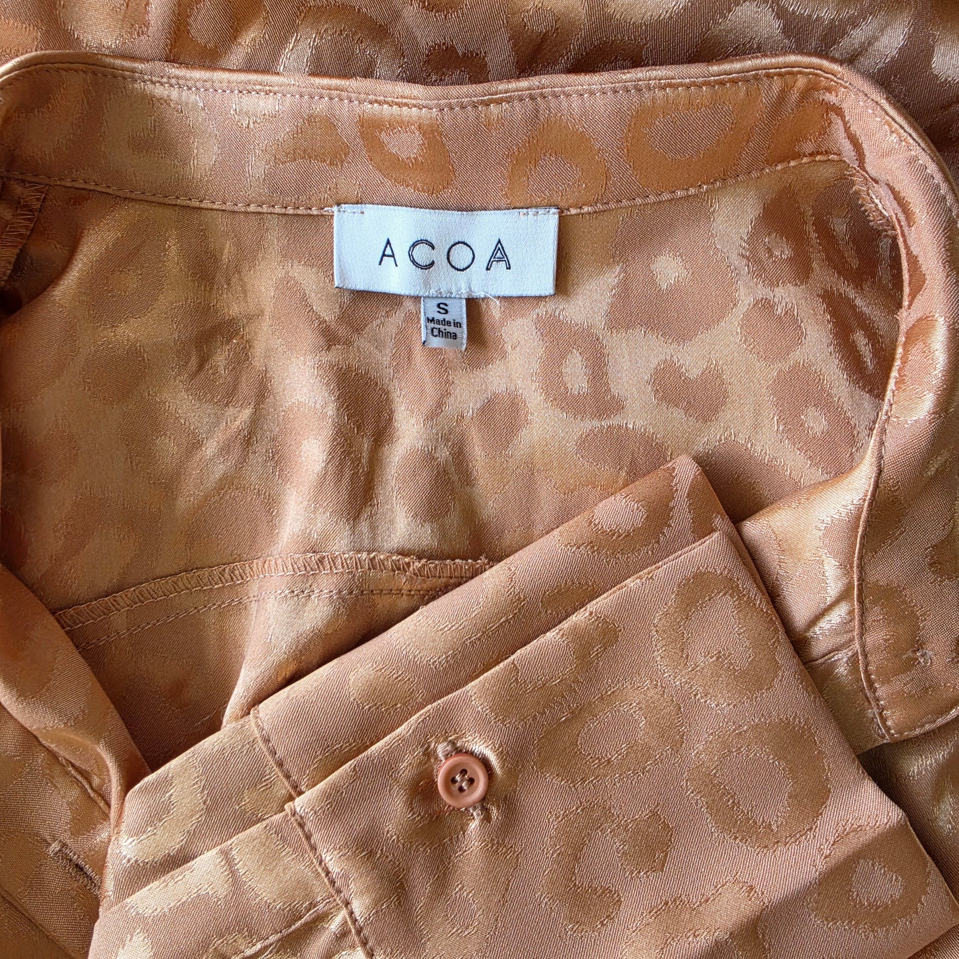 Close-up view of the brand label and shiny animal print pattern on the ACOA retro button up shirt.
