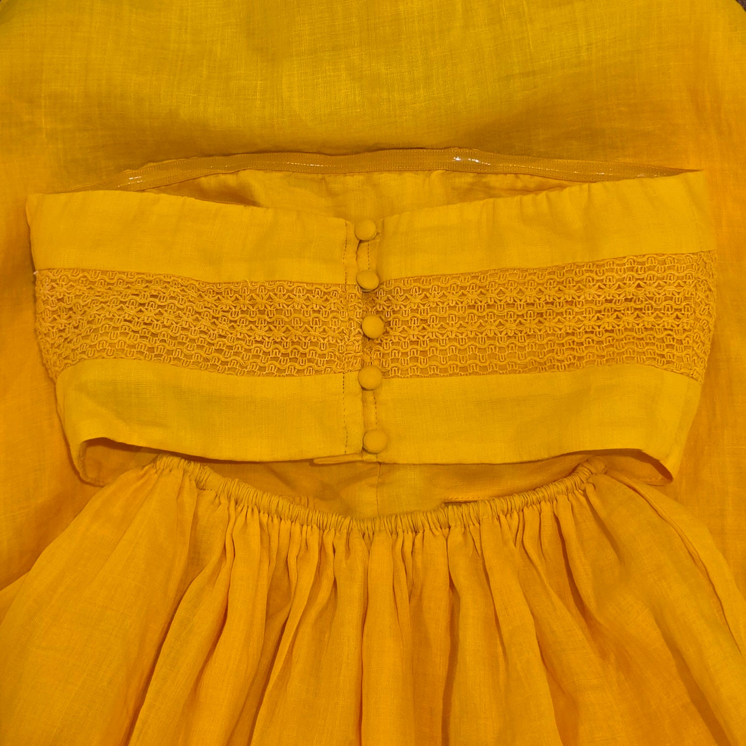 Back view of the Aere marigold strapless dress showing the textured bodice and button fastening.