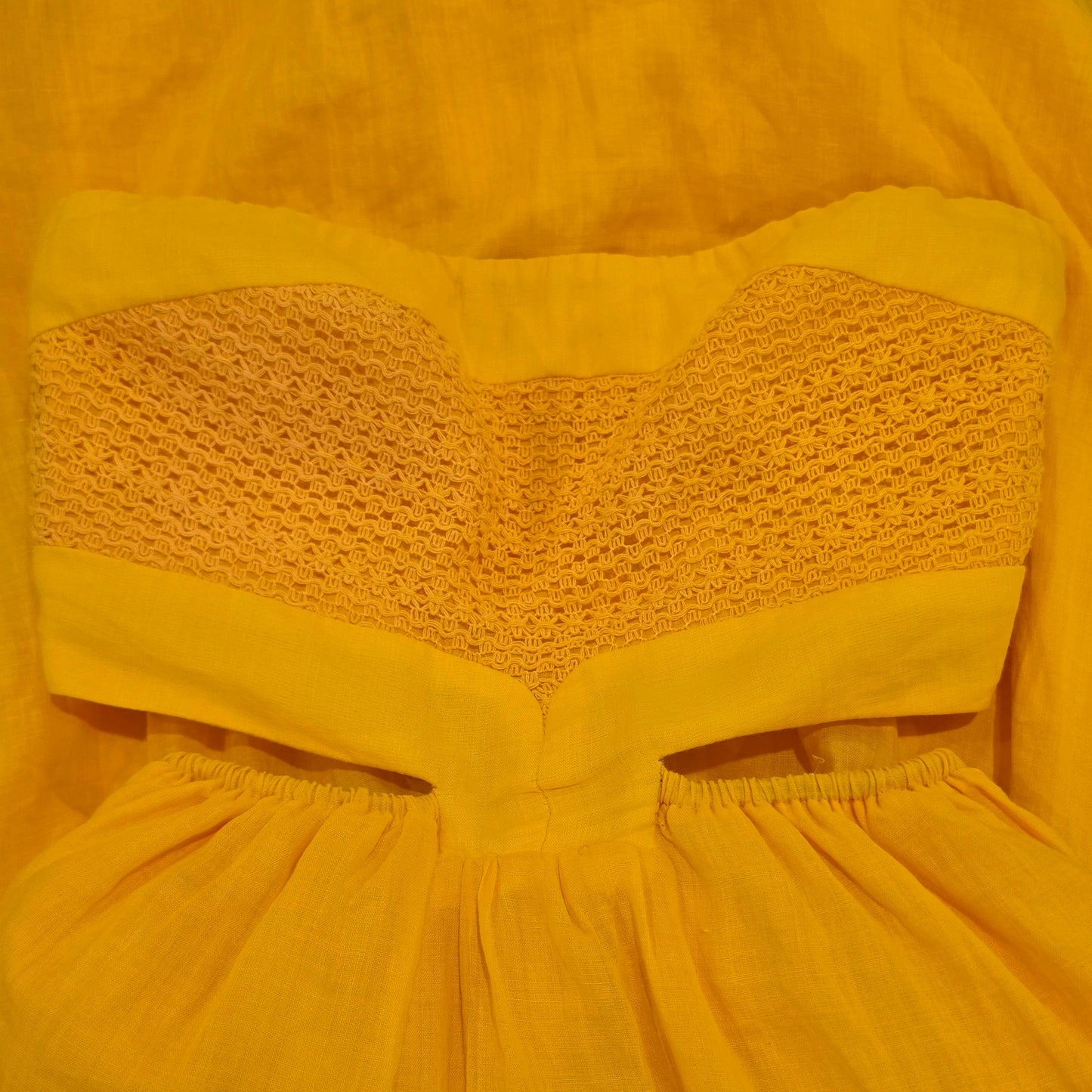 A close-up of the Aere yellow strapless dress featuring a textured crochet lace neckline and a gathered skirt.