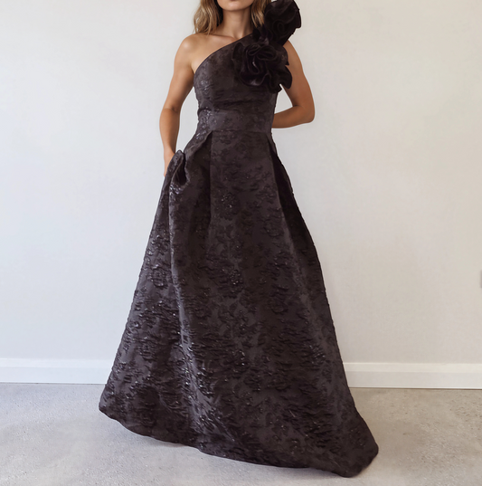 Anissa one-shoulder black jacquard ball gown with a dramatic oversized floral shoulder detail, fitted bodice and full-length voluminous skirt.