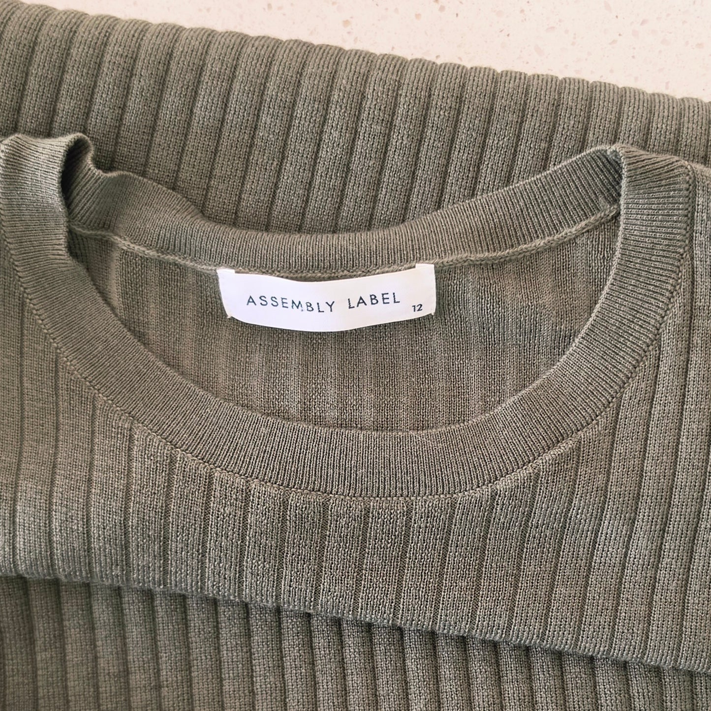 Close up view of the Assembly Label brand and size 12 on the ribbed midi dress.