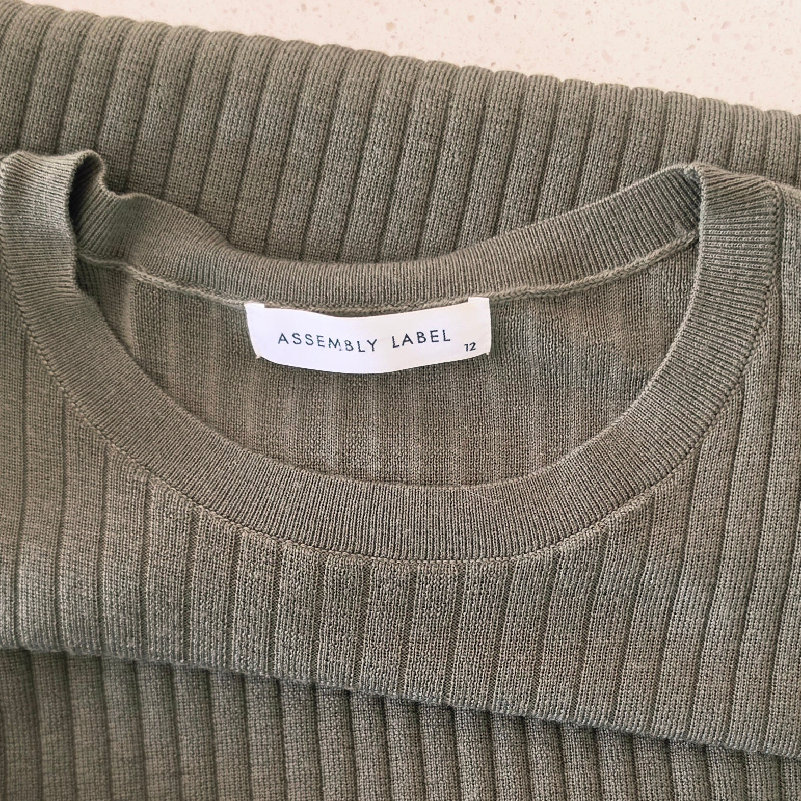 Close up view of the Assembly Label brand and size 12 on the ribbed midi dress.