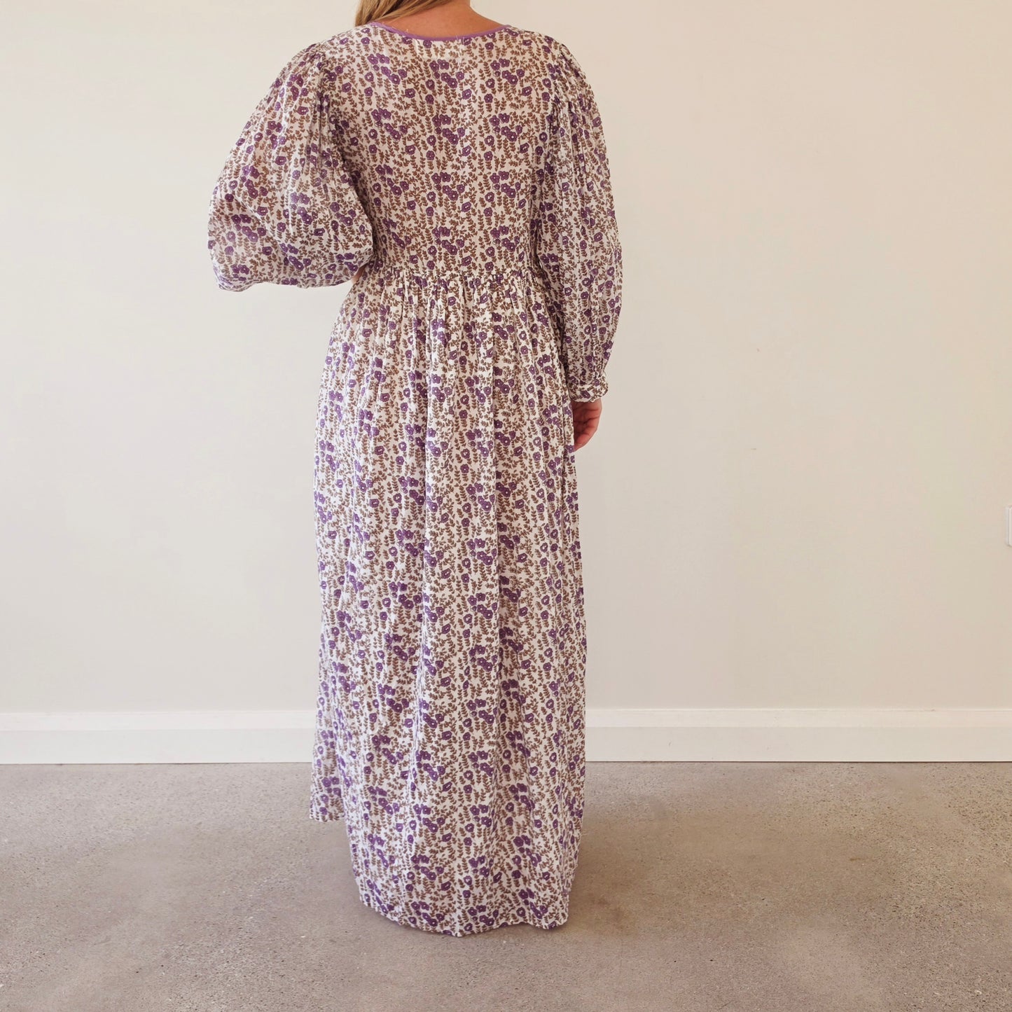 Back view of a woman wearing the Daughters of India long-sleeved Binita maxi dress with a purple and white abstract floral pattern and puff sleeves.