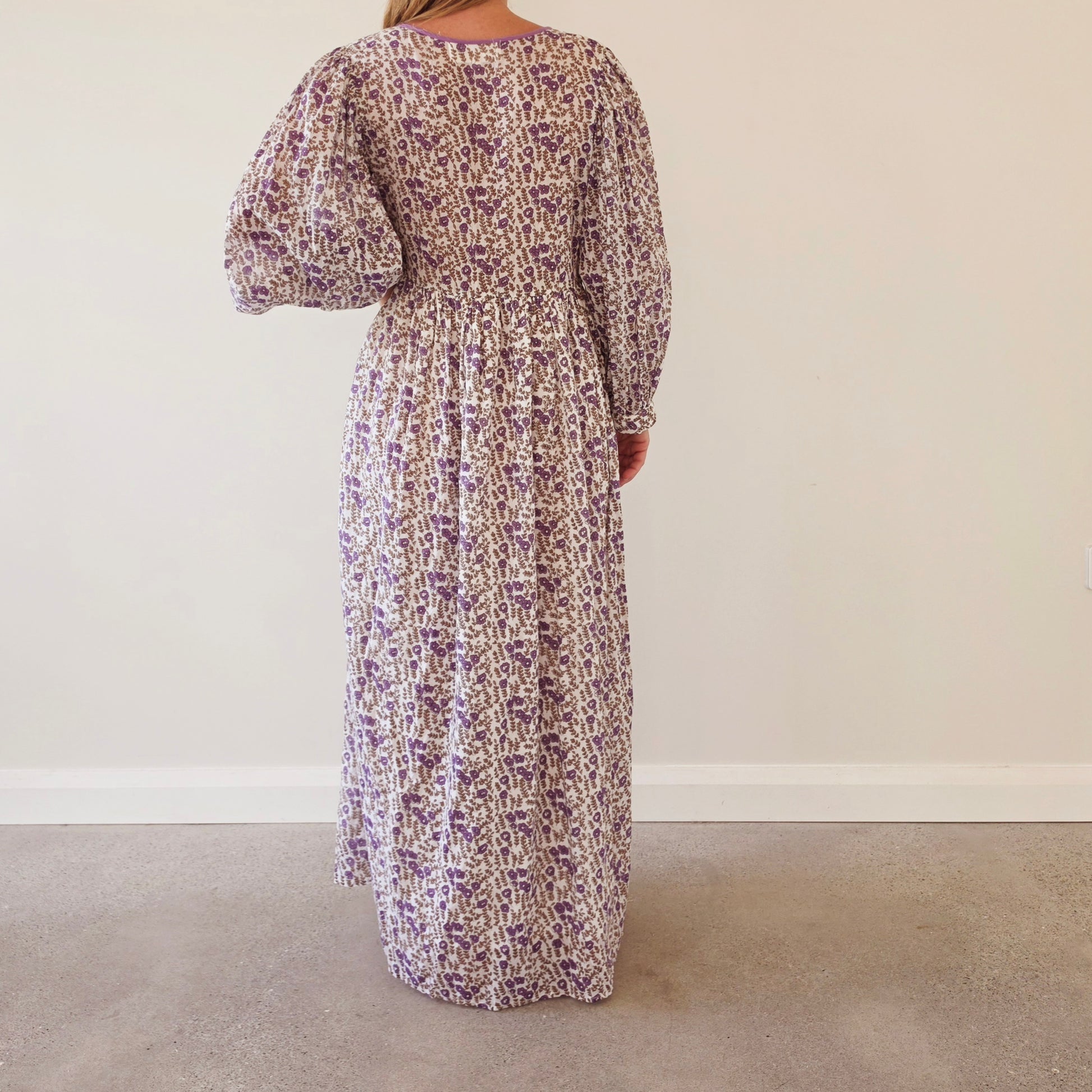 Back view of a woman wearing the Daughters of India long-sleeved Binita maxi dress with a purple and white abstract floral pattern and puff sleeves.