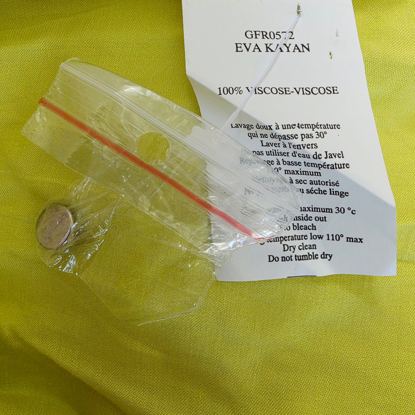 Close up view of the spare button and washing instructions on the Eva Kayan citrus coloured dress.