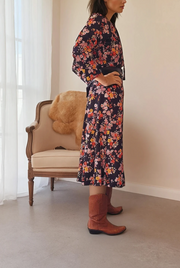 Gorgeous vintage black floral midi dress by Kitly Melbourne, this dress is in a polyester fabric, with longer sleeves and a neck tie. The floral print is scattered in in reds, yellows and dusty pinks on black. Available now online in a 16 at wilsonavenue.au