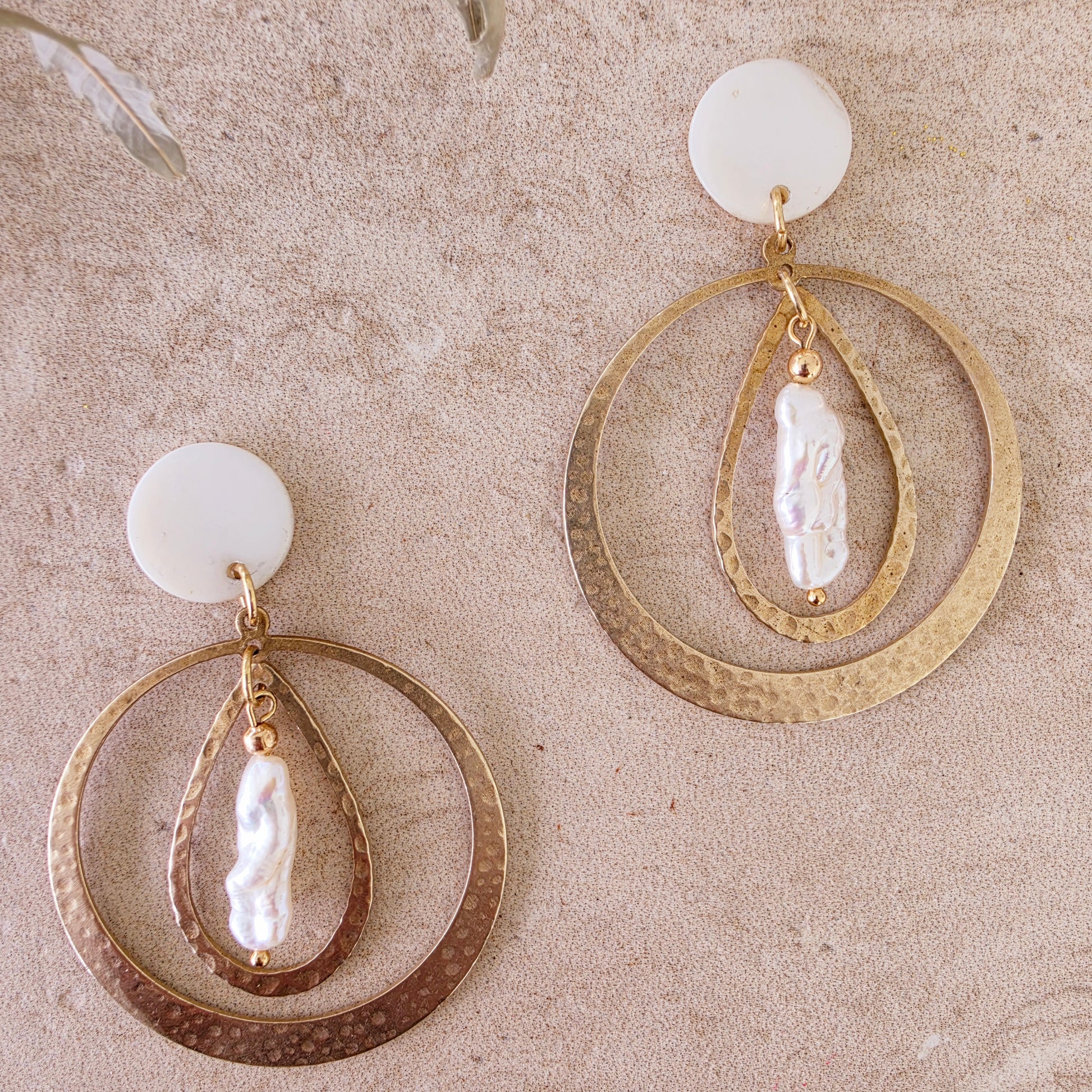 Close up view of the Kolekti pearl earrings, showing the hammered brass, mother of pearl and gold plated components.