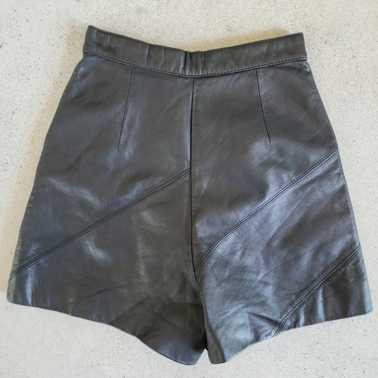 Back view of flatlay of black leather high waisted hot pants.