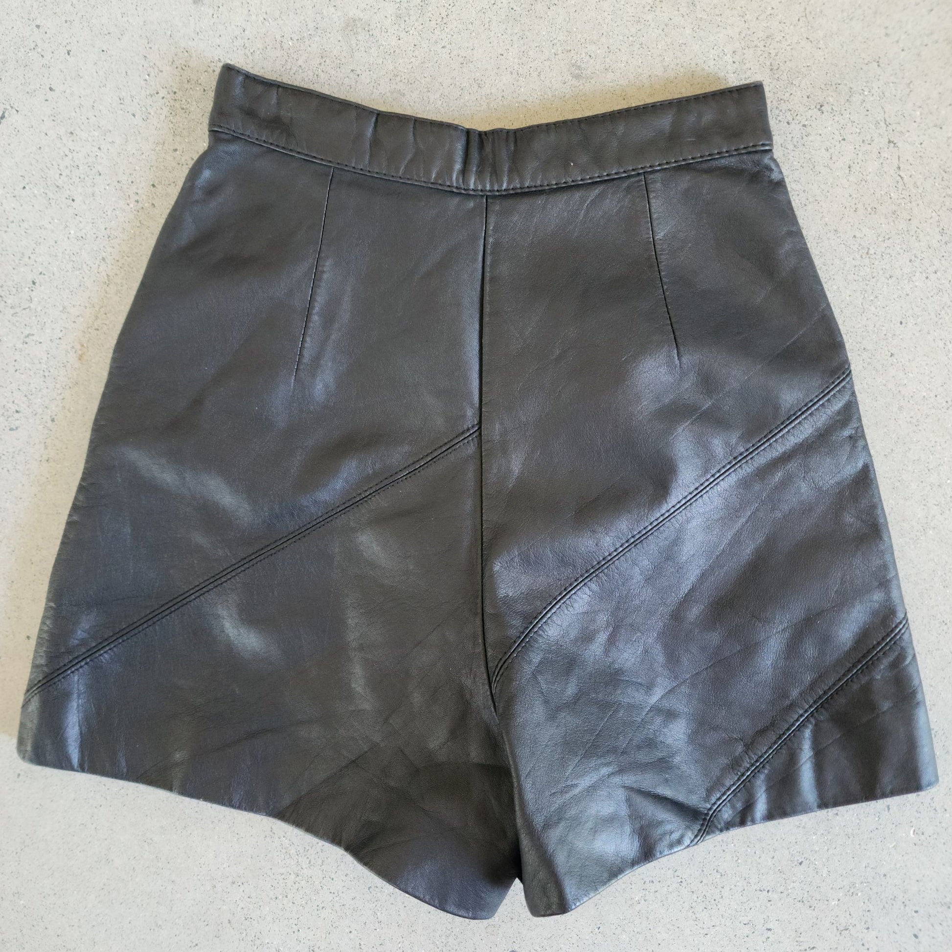 Back view of flatlay of black leather high waisted hot pants.