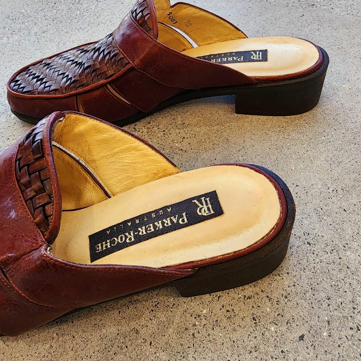 Close up side view of the back of the Parker Roche woven leather mules, showing the brand label and the maghogany colour.